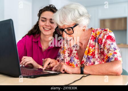 Beautiful grandmother and granddaughter together at home teaching how to use computer - Cheerful granma and nephew spending quality time together Stock Photo