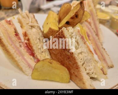 Delicious Club Sandwich with cheese, ham, tomato, egg, bacon and chicken accompanied by native potatoes Stock Photo