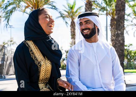 Traditional arab couple wearing emirati clothing dating outdoors - Middle-eastern married woman with abaya and man with kandura meeting and having fun Stock Photo