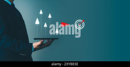 Businessman holding tablet that releases paper airplanes and the red paper airplane represents the difference that can reach the goal, Business target Stock Photo
