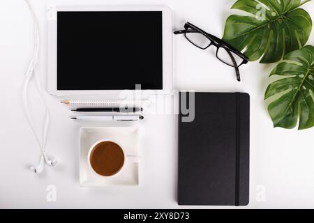 Modern white office desk table with tablet, eyeglasses, pen, pencil, ruler, monstera plant, notepad and greek cup of coffee. Top view, flat lay.Cope s Stock Photo