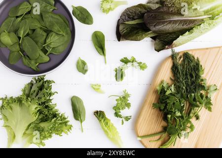 Flat lay with cutting board and bowl of fresh green salad leaves of spinach and lettuce, romaine and parsley, basil on white background. Healthy veget Stock Photo