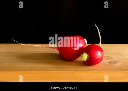 Two beautiful red radishes on a wooden board, on a black background. Stock Photo