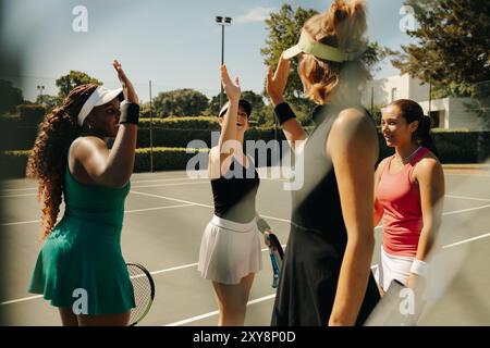 Group of women celebrating on a tennis court, waving and high-fiving each other after a successful team match. Happy and supportive sports environment Stock Photo