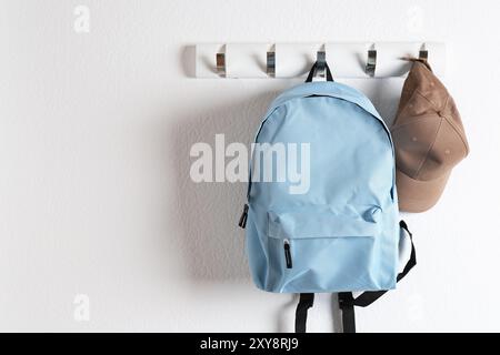 Light blue backpack and cap hanging on white wall, space for text Stock Photo