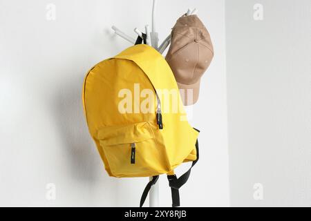 Yellow backpack and cap hanging on white wall Stock Photo