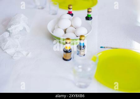 Close-up view of table with plates of Easter eggs ready for painting, surrounded by paint bottles, brush and glass of water. Sweden. Stock Photo