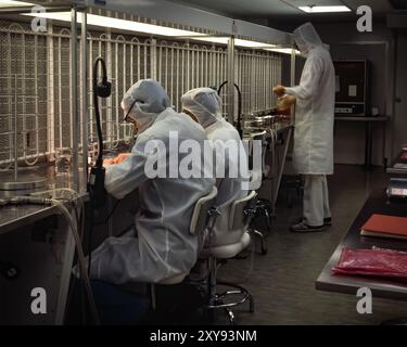 Scientists in full protective suits working at sterile laboratory fume hoods, handling samples in cleanroom environment with strict control. Stock Photo