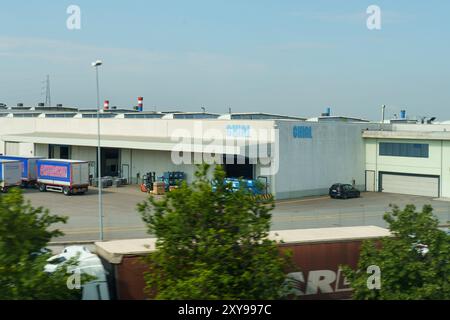 Camaione, Italy - June 8, 2023: A large industrial building in Italy, with delivery trucks and a car parked outside. Stock Photo