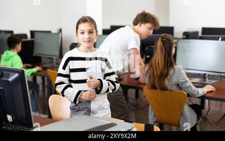 Teen schoolgirl with workbook in hands standing in computer class Stock Photo