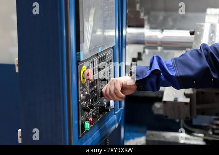 Operator controls CNC lathe machining center using control panel. Selective focus. Stock Photo