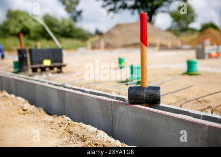 Close up of a rubber hammer standing on concrete curb stones, blurry background wit construction site workers  Stock Photo