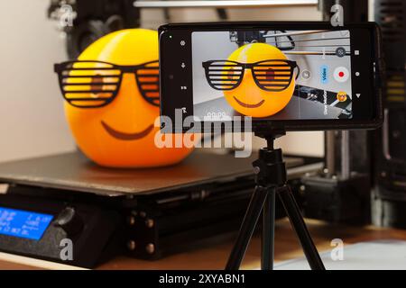 Phone camera monitoring a successful multi-colored 3d print of an emoji with 80's shutter shades on a 3d printer bed, with support material removed Stock Photo