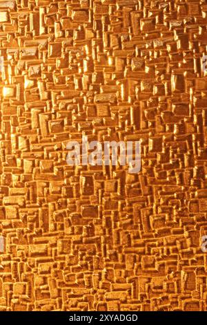 A close-up of shiny glass reflecting the warm, golden hues of sunset light. The abstract texture highlights the interplay of light and surface, creati Stock Photo