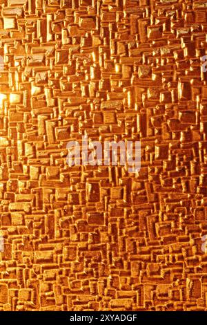 A close-up of shiny glass reflecting the warm, golden hues of sunset light. The abstract texture highlights the interplay of light and surface, creati Stock Photo