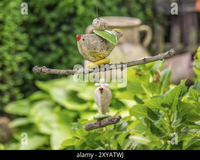 Filigree garden pendant in the shape of a bird on a branch, surrounded by green leaves and a rustic clay jug in the background, borken, muensterland, Stock Photo