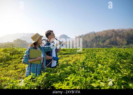 Indonesian farmers people are standing in a chili field, one of them pointing at something. They are both wearing hats and holding papers. Scene is pe Stock Photo