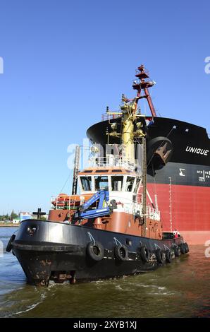 The oil tanker Unique Guaridan is towed in the harbour basin by a tugboat. Oil tanker towaged in harbour Stock Photo