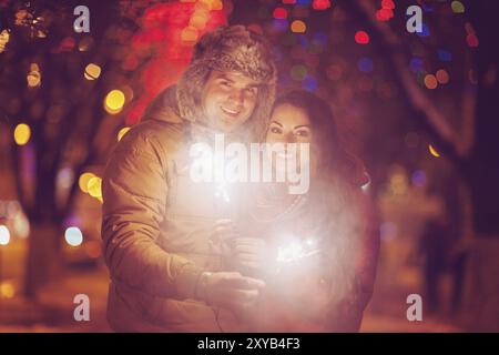 Young couple with Bengal light looking at camera outside over Christmas background Stock Photo