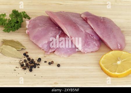 Three pieces of raw meat on a wooden board, turkey steak with spices before cooking Stock Photo