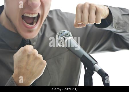 Businessman screaming in microphone with his fist rased up isolated on white background, shallow depth of field with focus placed on mike Stock Photo