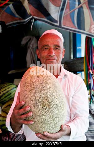 Portrait of an Uyghur man holding a melon at the market in Kashgar, Xinjiang, China. Stock Photo