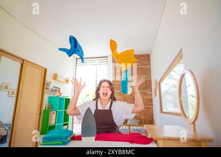 An Indonesian housewife is in a room with a pile of clothes and a pile of towels. She is yelling and seems to be in a bad mood Stock Photo
