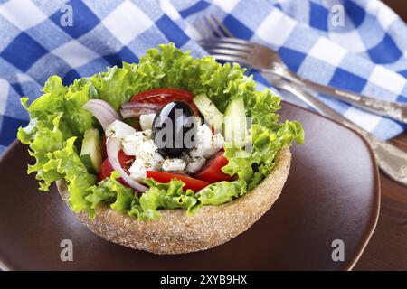 Close up of Greek salad in a bowl of whole-grain bread on wooden table, selective focus Stock Photo