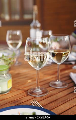 Glass goblets with white wine placed on wooden table during romantic dinner in yard Stock Photo