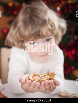 Happy child holding cookies against Christmas lights background Stock Photo