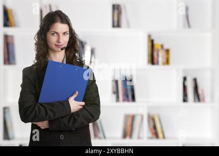 Corporate woman talking over her headset, holding a blue pad Stock Photo