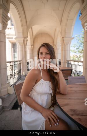 Woman White Dress Balcony Arches - A woman in a white dress sits on a balcony surrounded by arches. Stock Photo