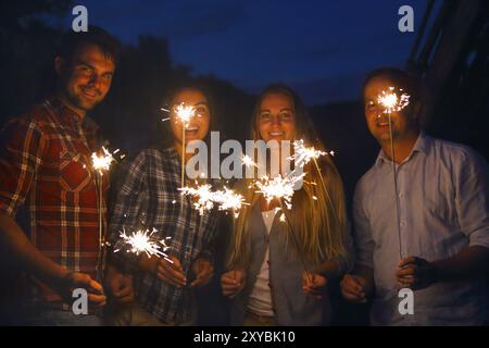 Young happpy people with sparklers having fun on outdoor party Stock Photo