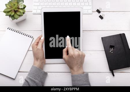 Female hands over desktop blogger or business woman holding a tablet. Flat lay, overhead view Stock Photo