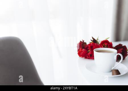 Red tulips bouquete on table, white coffee cup. Concept for greeting card for mothers day, international womans day or valentines day concept, birthda Stock Photo