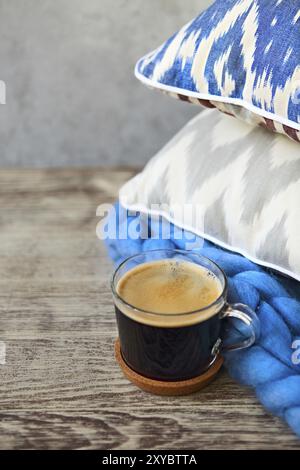 Blue and grey pillows with blanket and cup of coffee on the wooden background. Close up Stock Photo