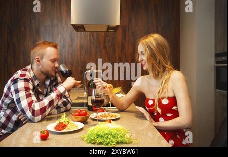 Happy woman eating pasts while man tasting red wine in a kitchen. Couple on the date Stock Photo