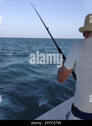 Young man fishing on a ocean. Catching big Queen fish Stock Photo