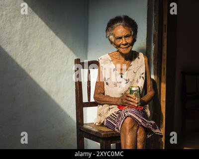 Baracoa, Cuba on January 7, 2016: In a Cuban house an old woman is enjoying a beer in the sun Stock Photo