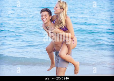 Happy man carrying his girlfriend on his back having fun on the beach Stock Photo