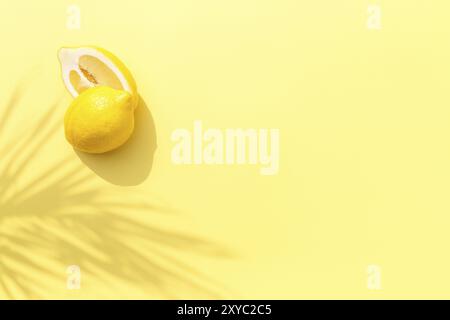 Two halved cuts of lemon with shadow from palm leaf on yellow background. Healthy eating, travel or vacation concept Stock Photo