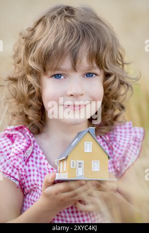 Child holding house in hands against autumn yellow background. Real estate concept Stock Photo