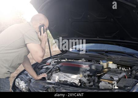 Close up of a broken down car, engine open and smoking, in a rural area and the driver looking at the engine Stock Photo