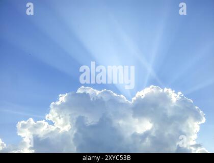 The sun is hiding behind a cumulus cloud towards clear blue sky Stock Photo