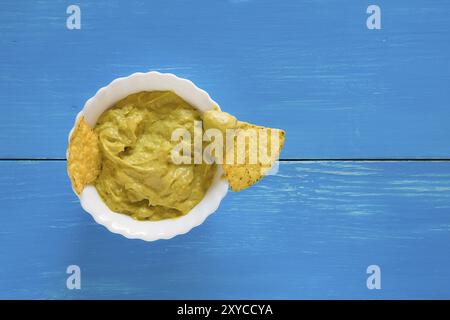 Nachos chips dipping in salsa guacamole over a blue background seen from above Stock Photo