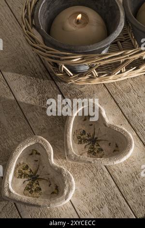 Two decorative hears made from stone ware in the shape of little cups or holders on a white whashed wooden table next to a burning ball candle in a po Stock Photo