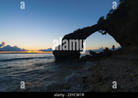 The sunset glows orange below the horizon behind the natural bridge and rocky beach landmarks of Neil Island of the Andaman and Nicobar Islands of Ind Stock Photo