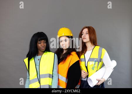 Three women are posing in their safety vests and hard hats with blueprints under their arm Stock Photo