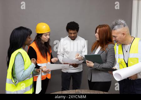 Diverse team of architects and engineers are gathered together, reviewing blueprints and discussing a project Stock Photo