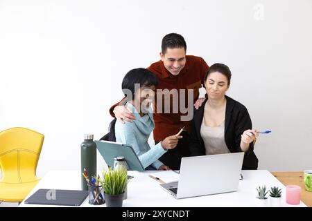 Three businesspeople working together in the office, brainstorming and discussing ideas for a new project, using a laptop and smiling Stock Photo
